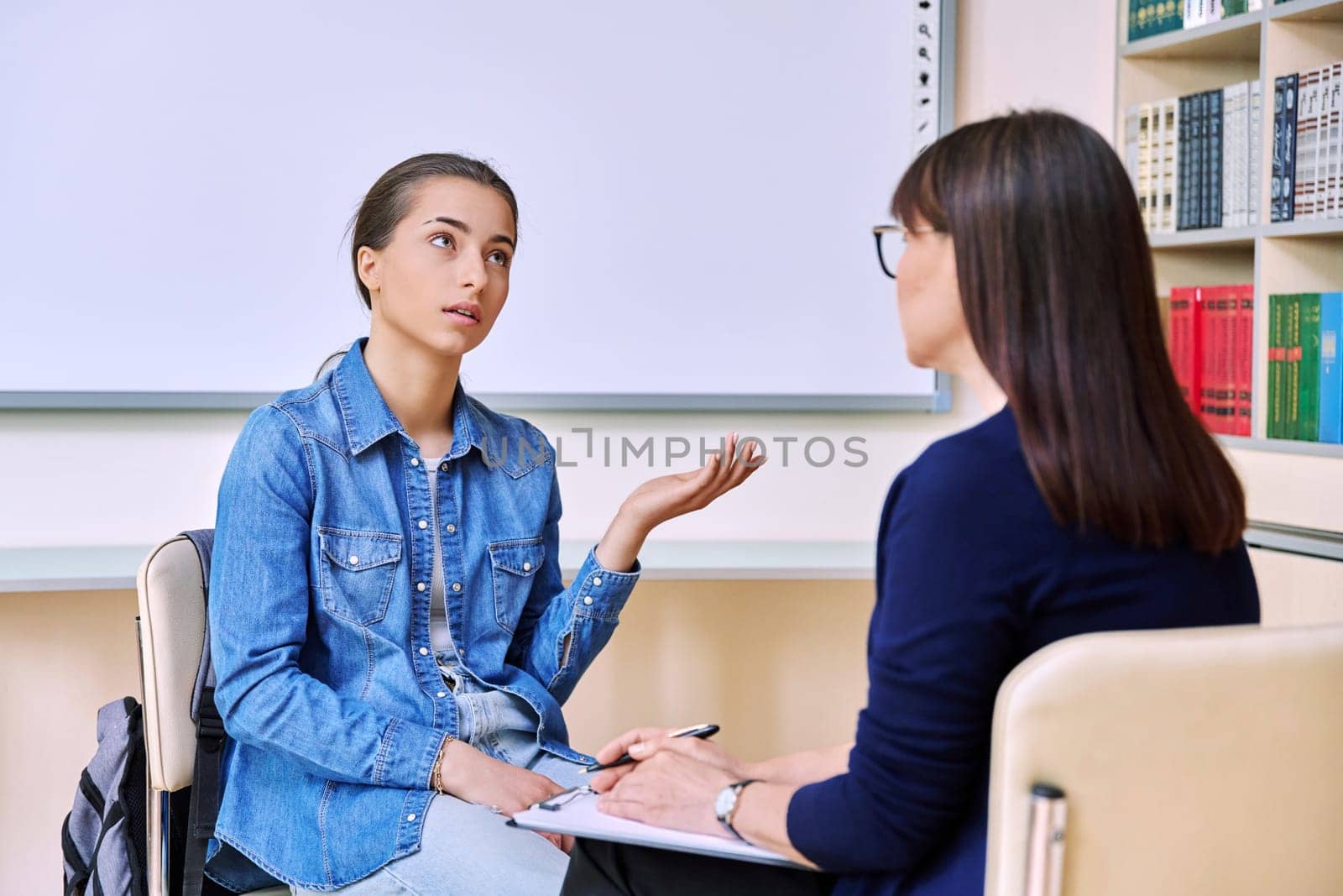 Psychologist consulting on behavior talks with serious teenage girl inside educational building in office. Social service, educational counselor mentor teacher psychotherapist, students adolescence