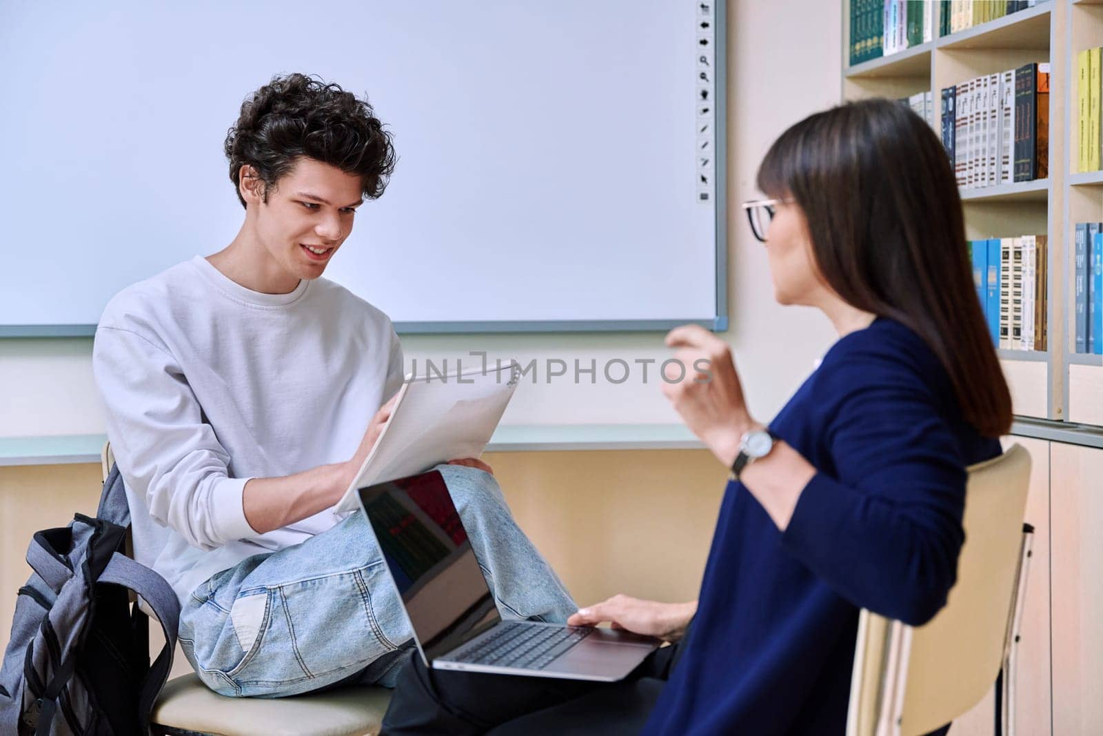 Guy college student talking studying with female teacher. Mentor and student together in the classroom. Education, training, mentoring, teaching, youth concept