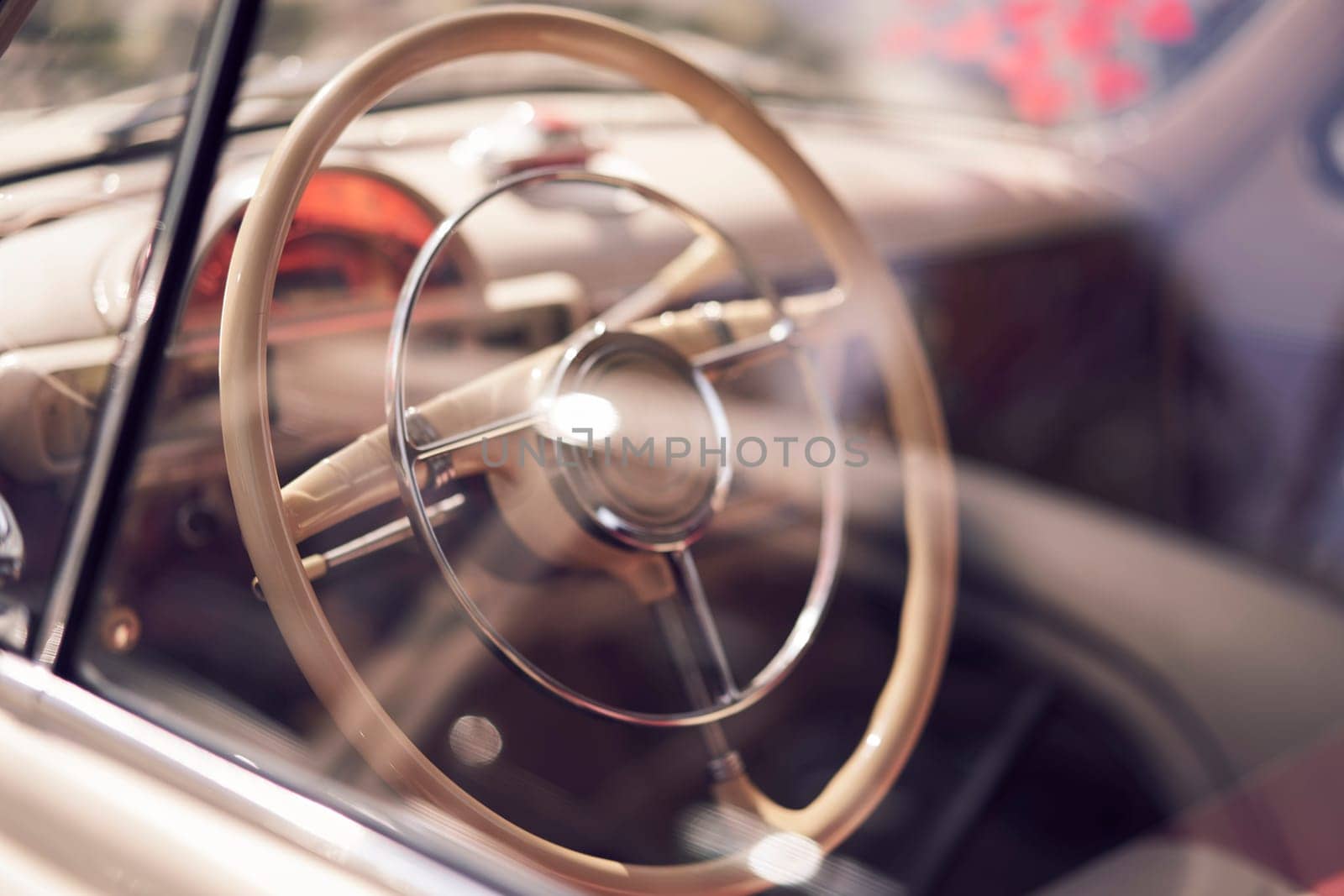 A vintage cars steering wheel and classic dashboard can be seen through the car window in a closeup view