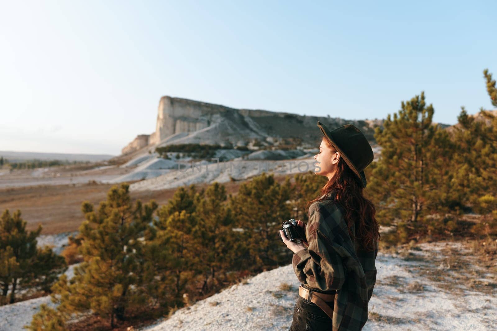 Woman in a hat and plaid shirt admiring rocky landscape from hilltop by Vichizh