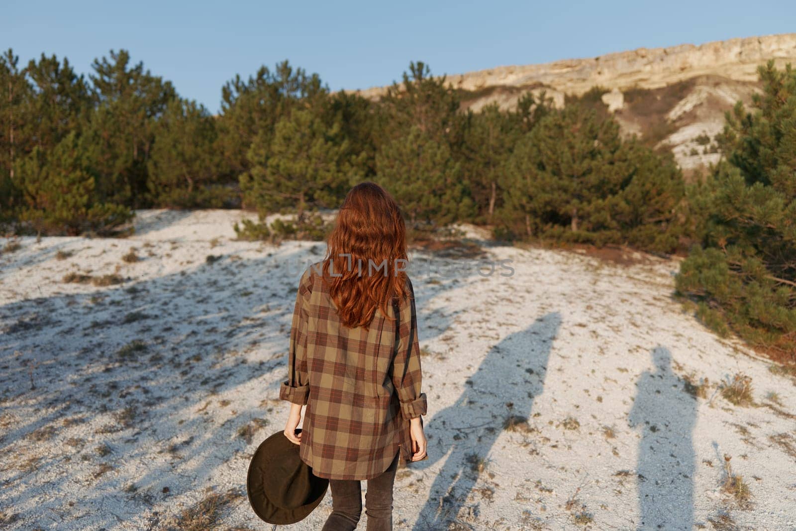 Winter wanderlust stylish woman in plaid shirt and hat stands in snowy landscape with rolling hills