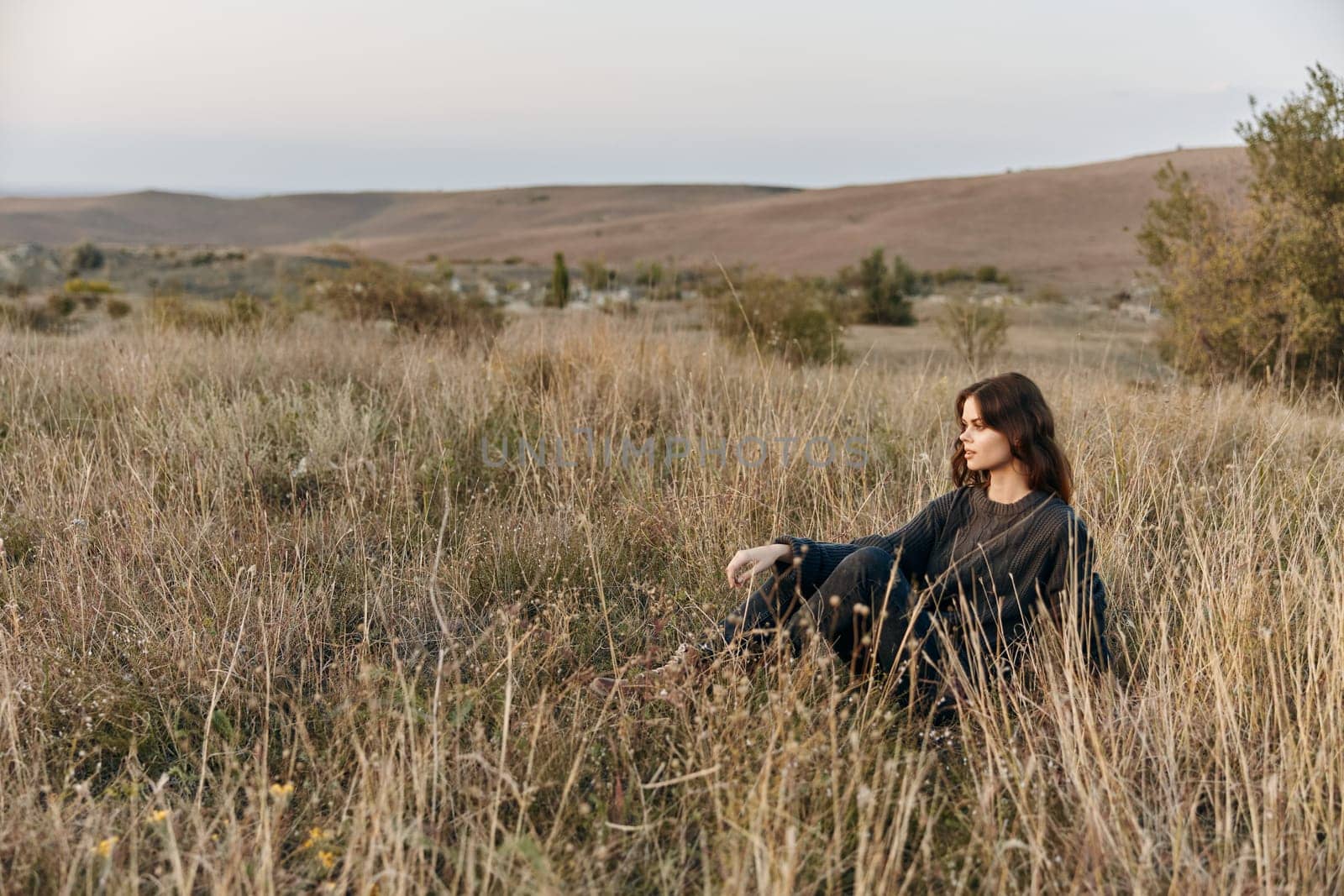 Serene woman sitting in tall grass with majestic mountains in the background on a sunny day