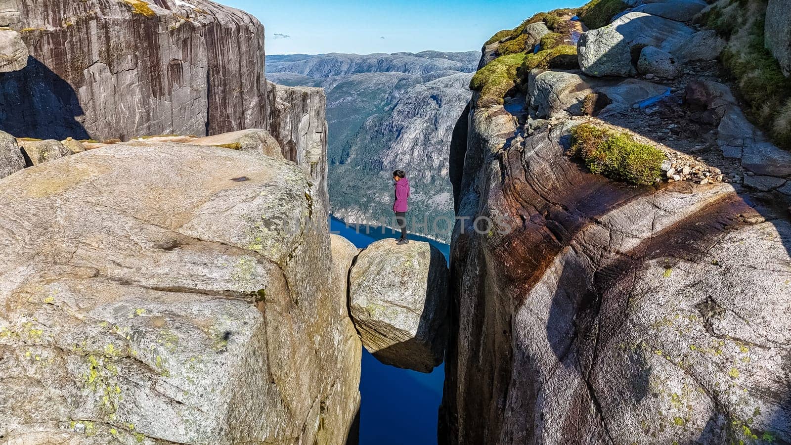 A lone hiker stands on the edge of the iconic Kjeragbolten cliff in Norway, gazing out at the breathtaking landscape below by fokkebok