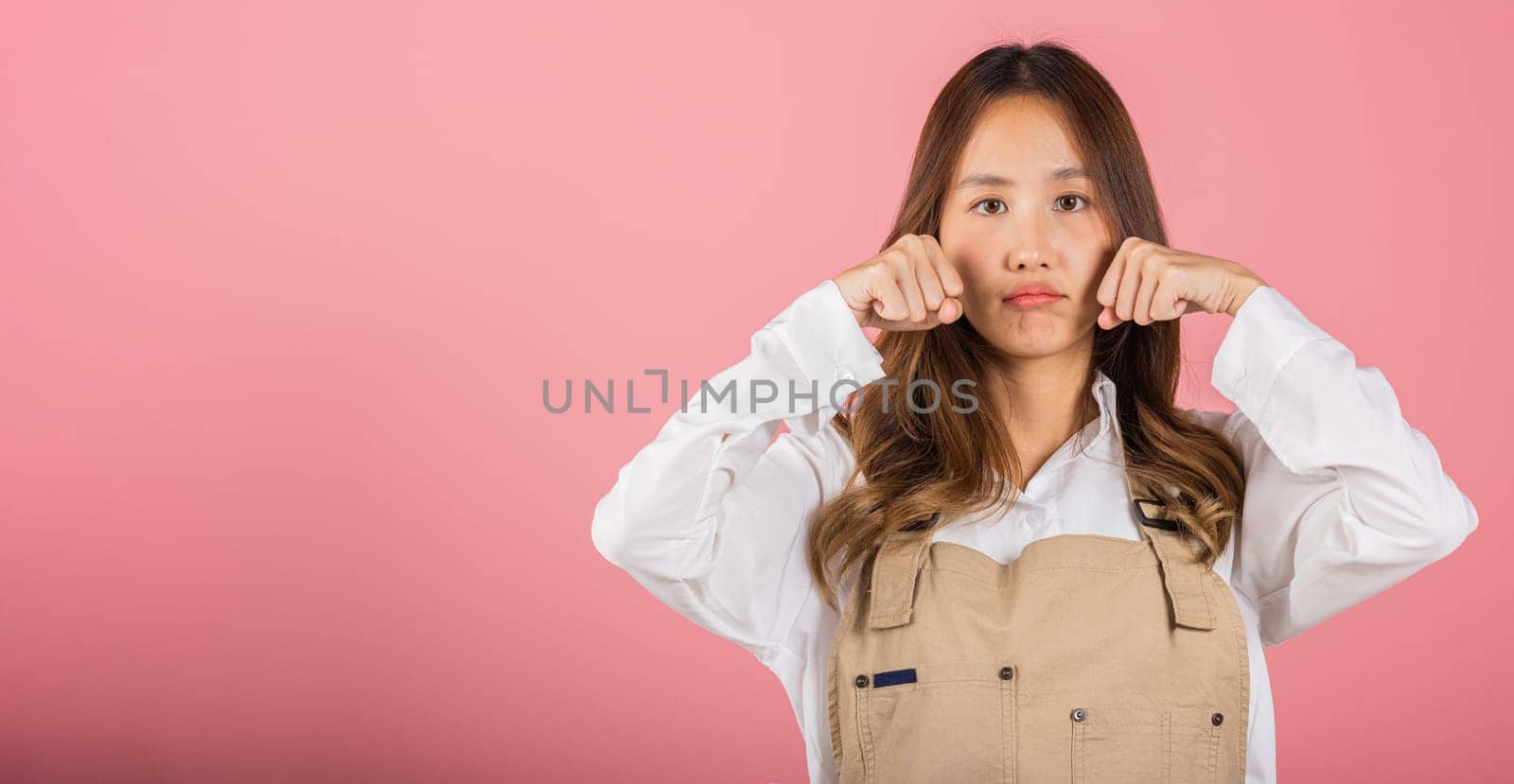 Unhappy small business woman bad mood her cry wipe tears with fingers, Asian beautiful young female stress feeling sad unhappy crying, studio shot isolated on pink background with copy space