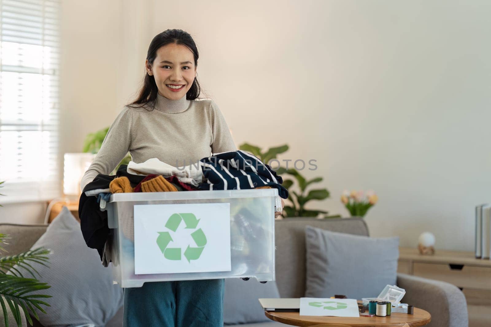 A young woman holding a recycling bin filled with clothes, emphasizing the importance of recycling and sustainable living in a modern home setting.