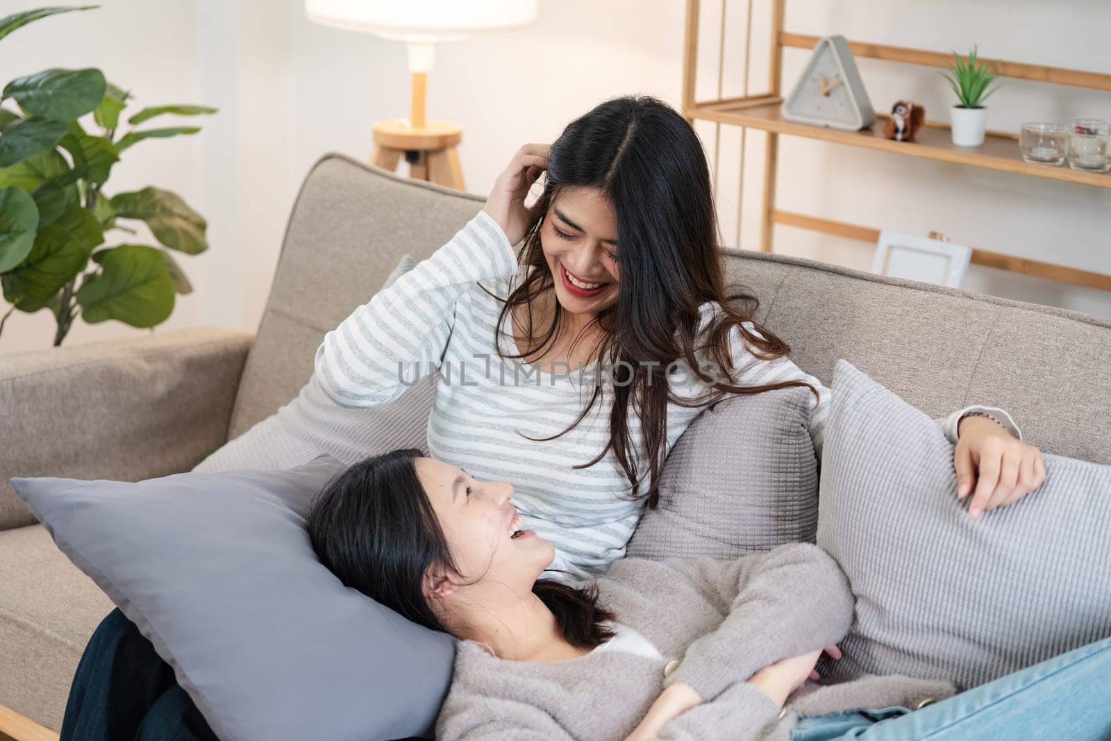 Young smiling gay couple in casual wear spend time together while sitting on couch in cozy living room.