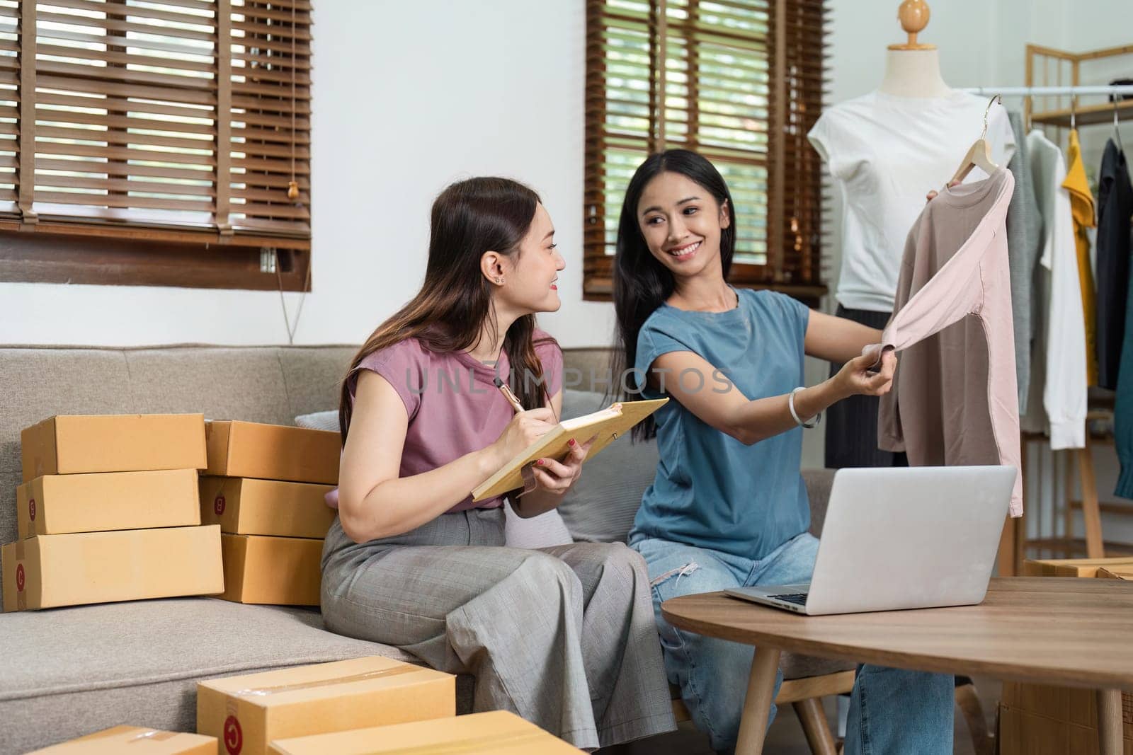 Two young women managing an online business from home, discussing orders, and packing products. Modern e-commerce concept.
