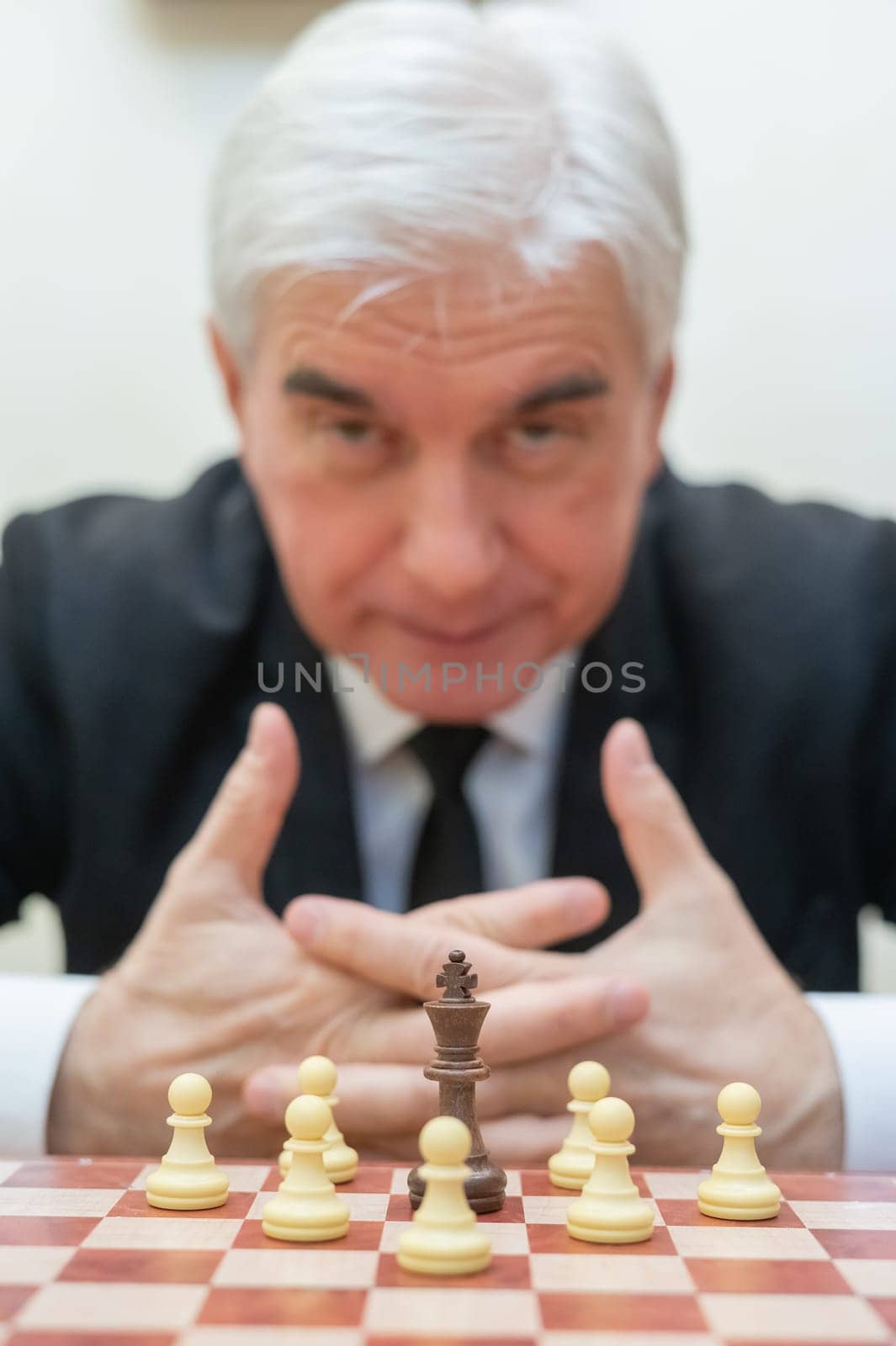 Elderly Caucasian man looking at camera while playing chess. Vertical photo. by mrwed54