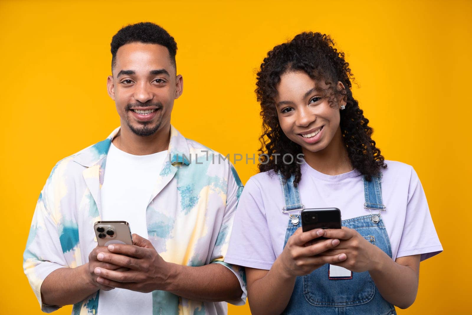 Two hipster friends smiling cheerfully while standing against a yellow background. High quality photo