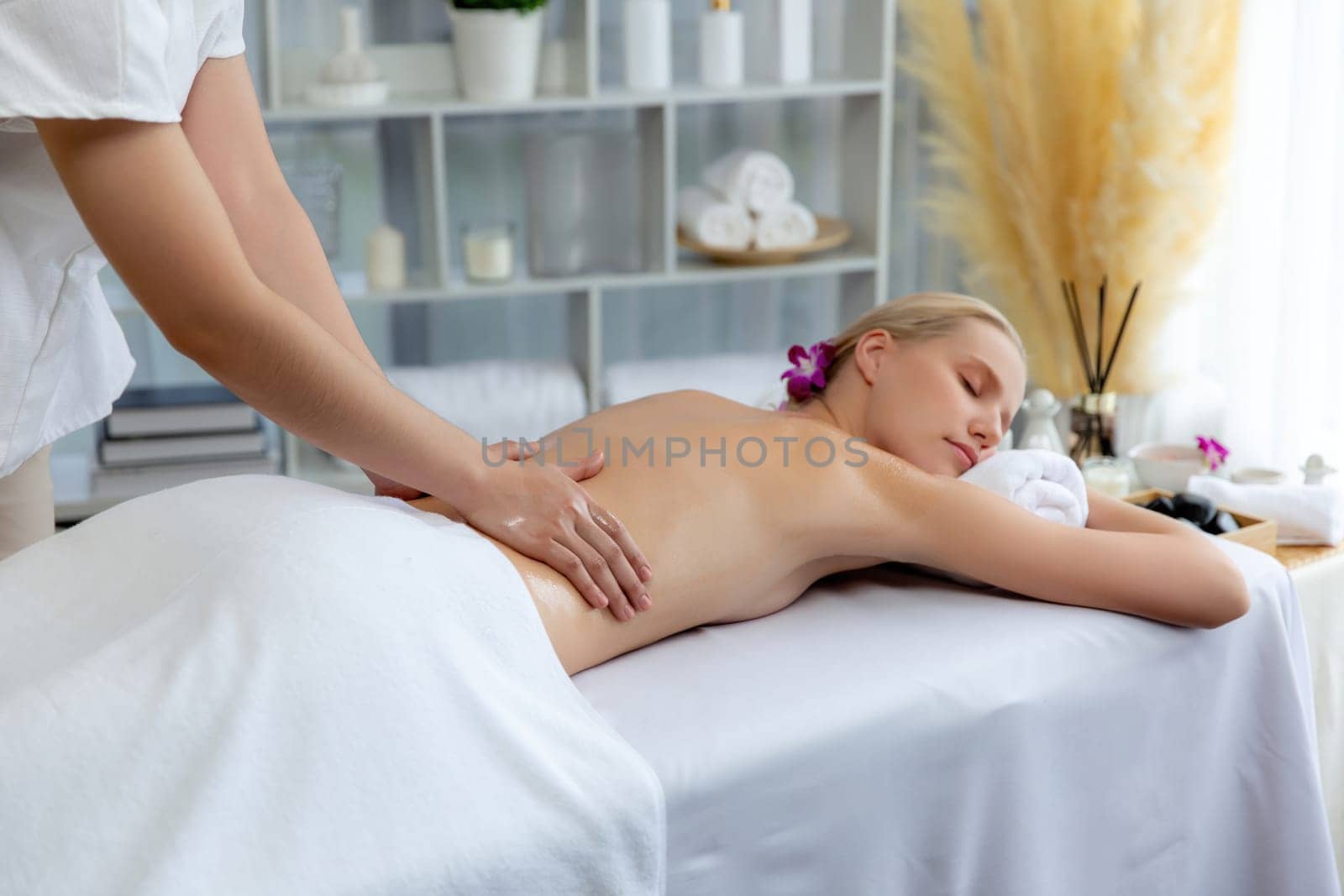 Caucasian woman customer enjoying relaxing anti-stress spa massage and pampering with beauty skin recreation leisure in day light ambient salon spa at luxury resort or hotel. Quiescent