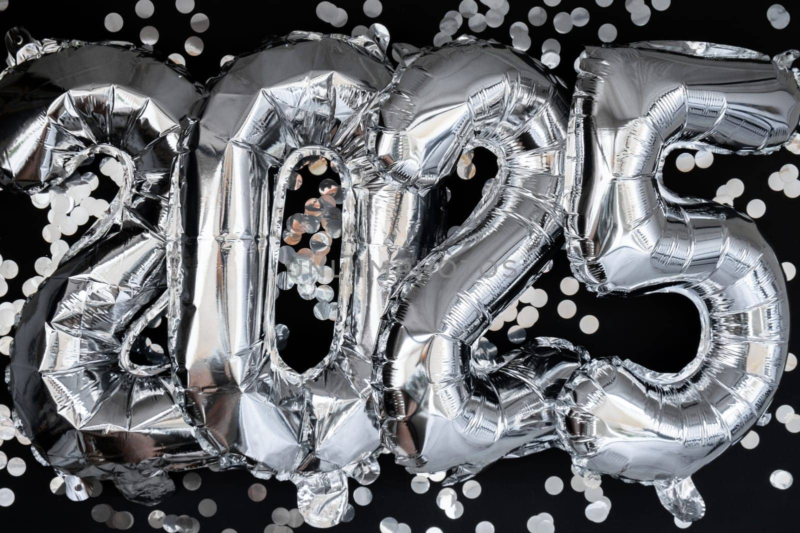 Happy new year 2025 metallic balloons with confetti on dark black background. Greeting card silver foil balloons numbers Christmas holiday concept. Celebration party congratulation decoration
