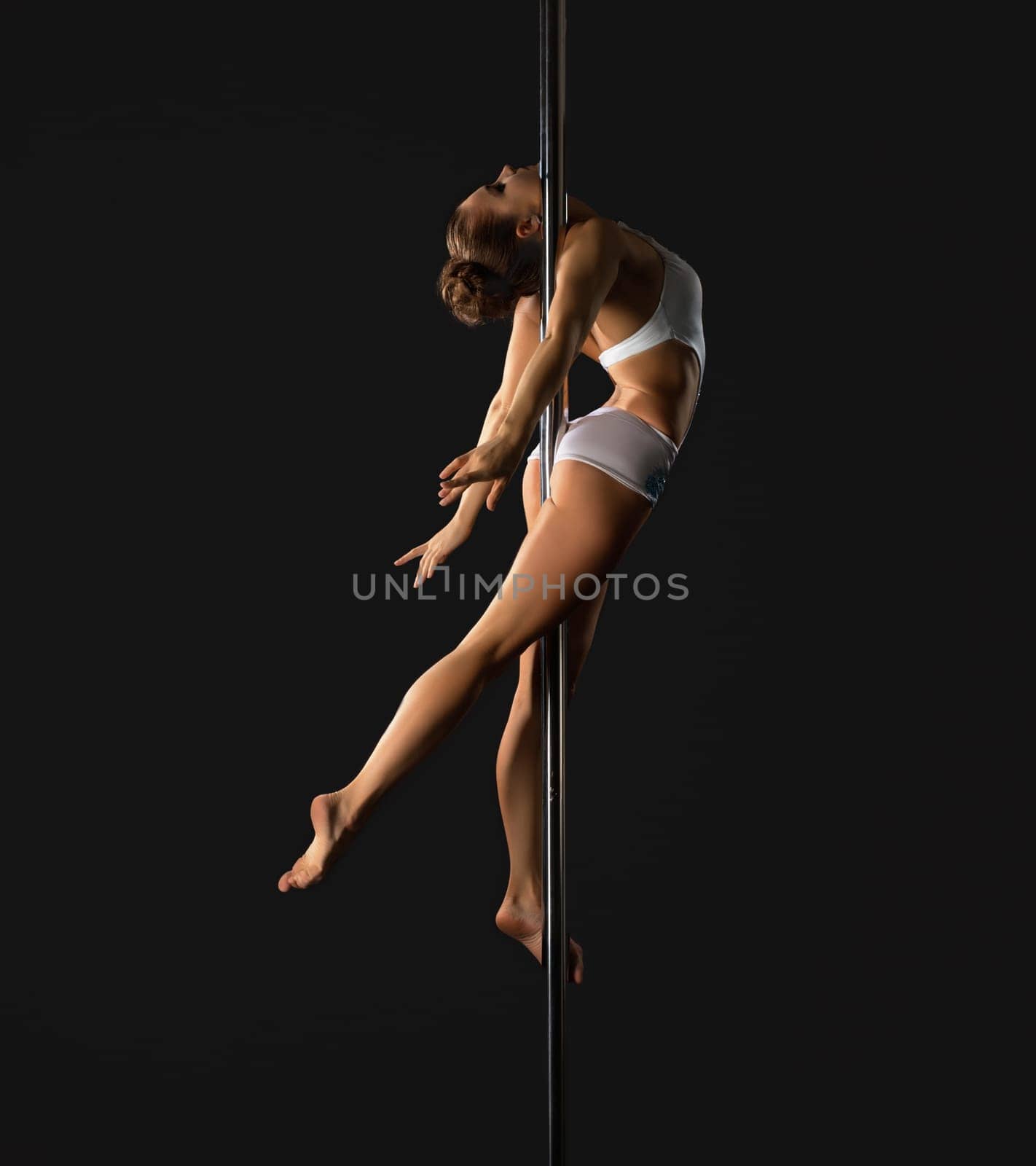 Young brunette girl in nice costume making exercises on pylon in studio