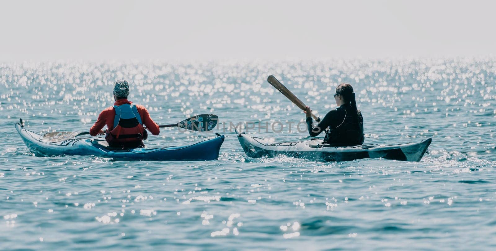 Happy smiling woman in kayak on ocean, paddling with wooden oar. Calm sea water and horizon in background