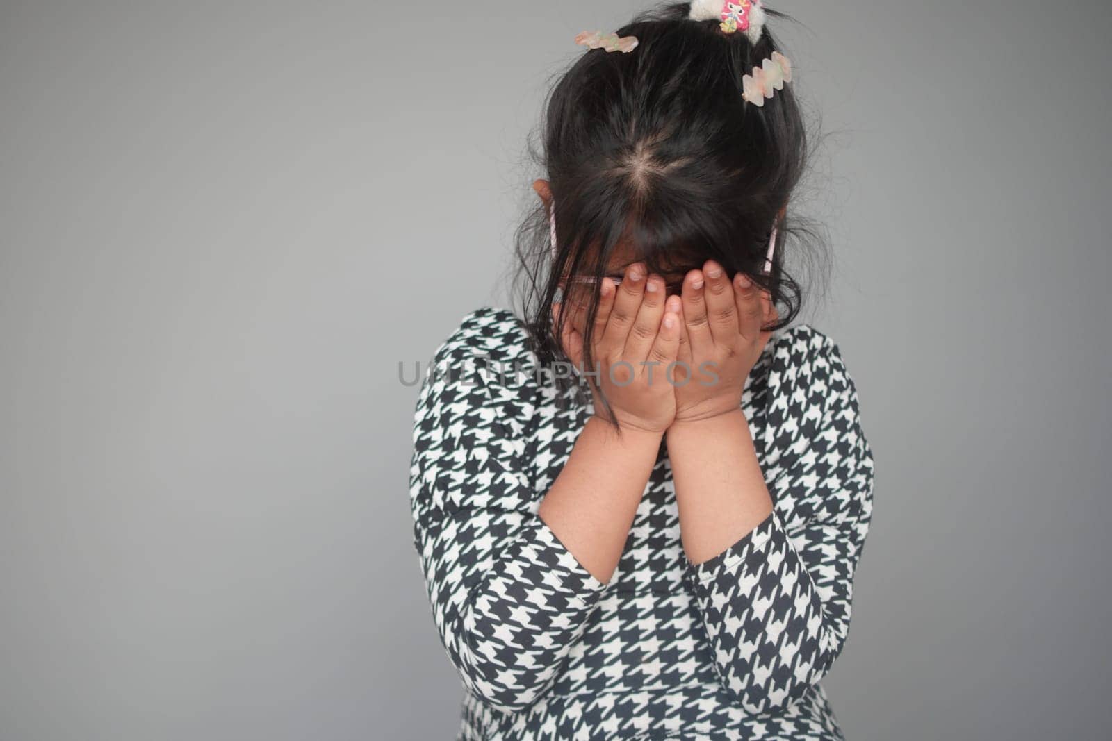 a upset child girl cover her face with hand .