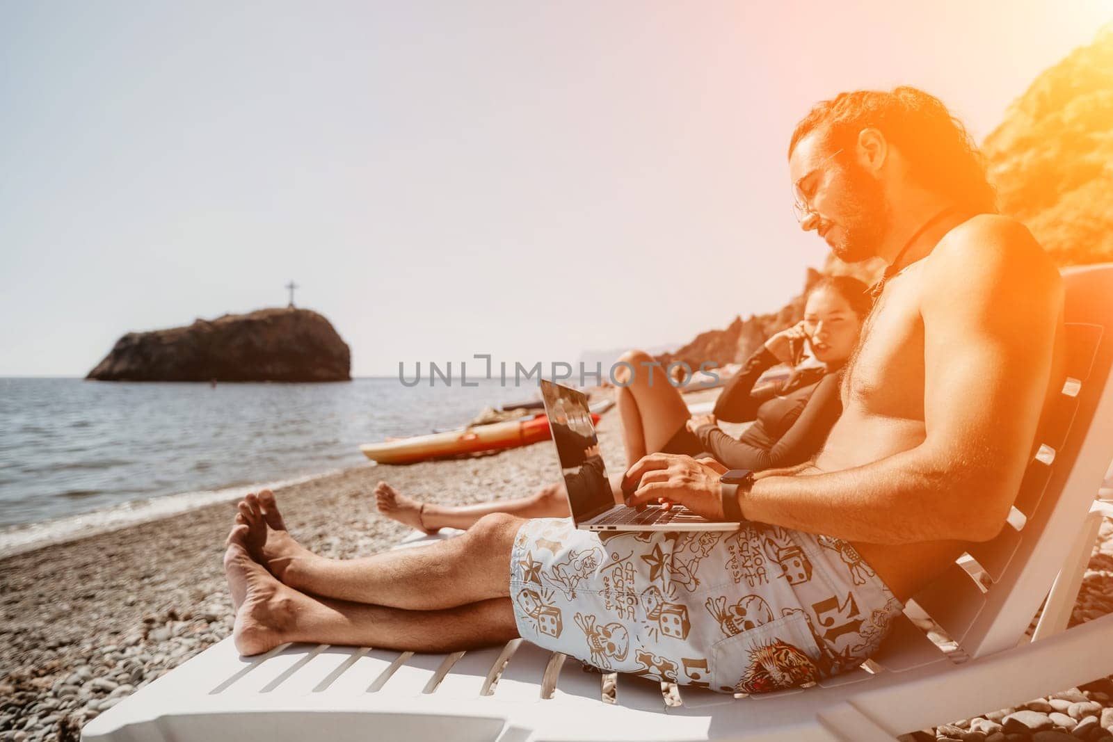 Digital nomad, Business man working on laptop by the sea. Man typing on computer by the sea at sunset, makes a business transaction online from a distance. Freelance, remote work on vacation