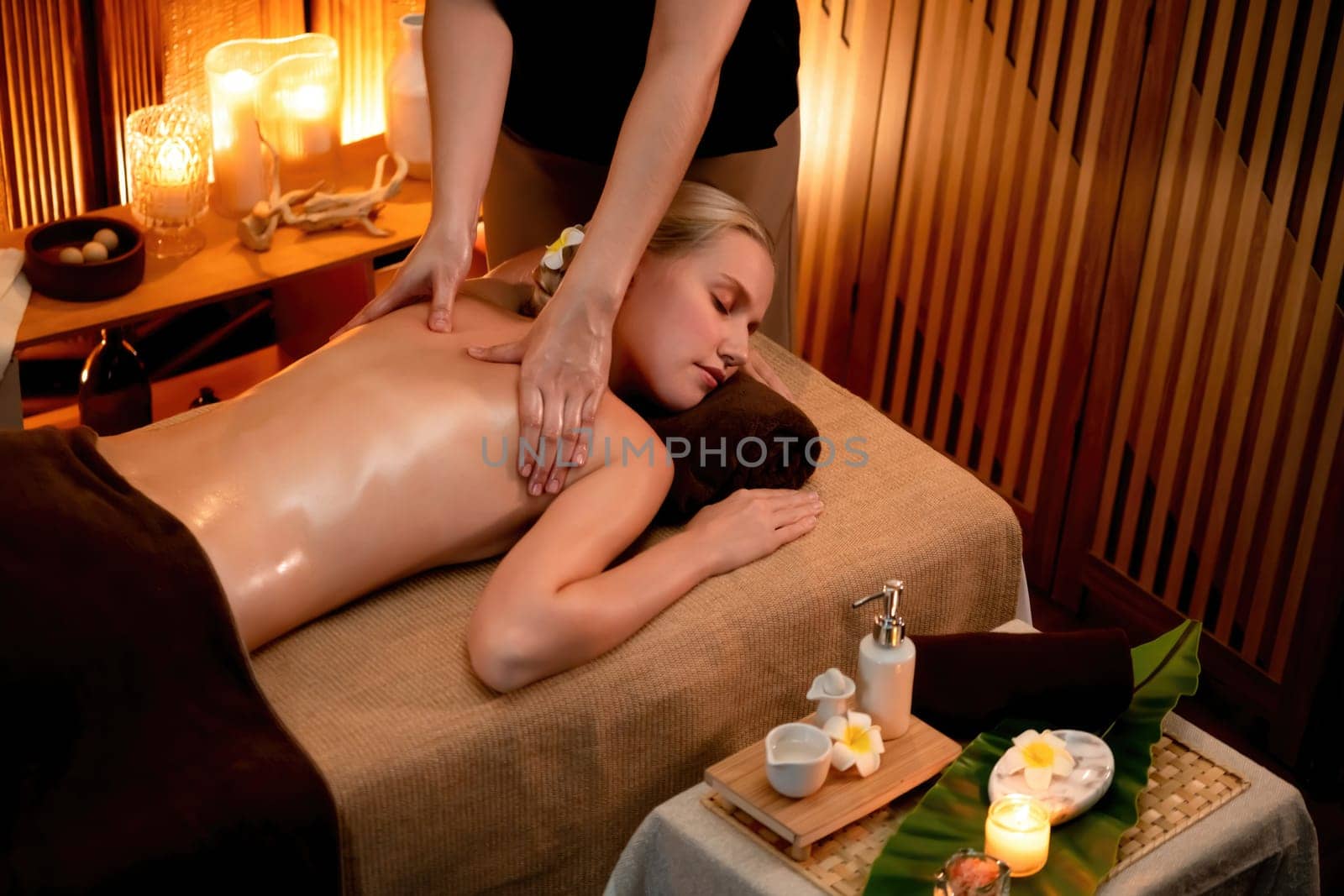 Caucasian woman customer enjoying relaxing anti-stress spa massage and pampering with beauty skin recreation leisure in warm candle lighting ambient salon spa at luxury resort or hotel. Quiescent