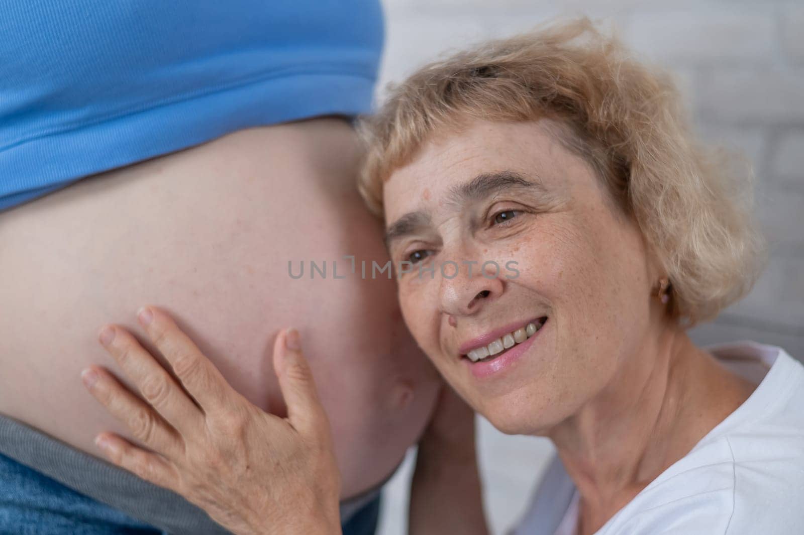 An elderly woman leans against the belly of her pregnant daughter. Close-up