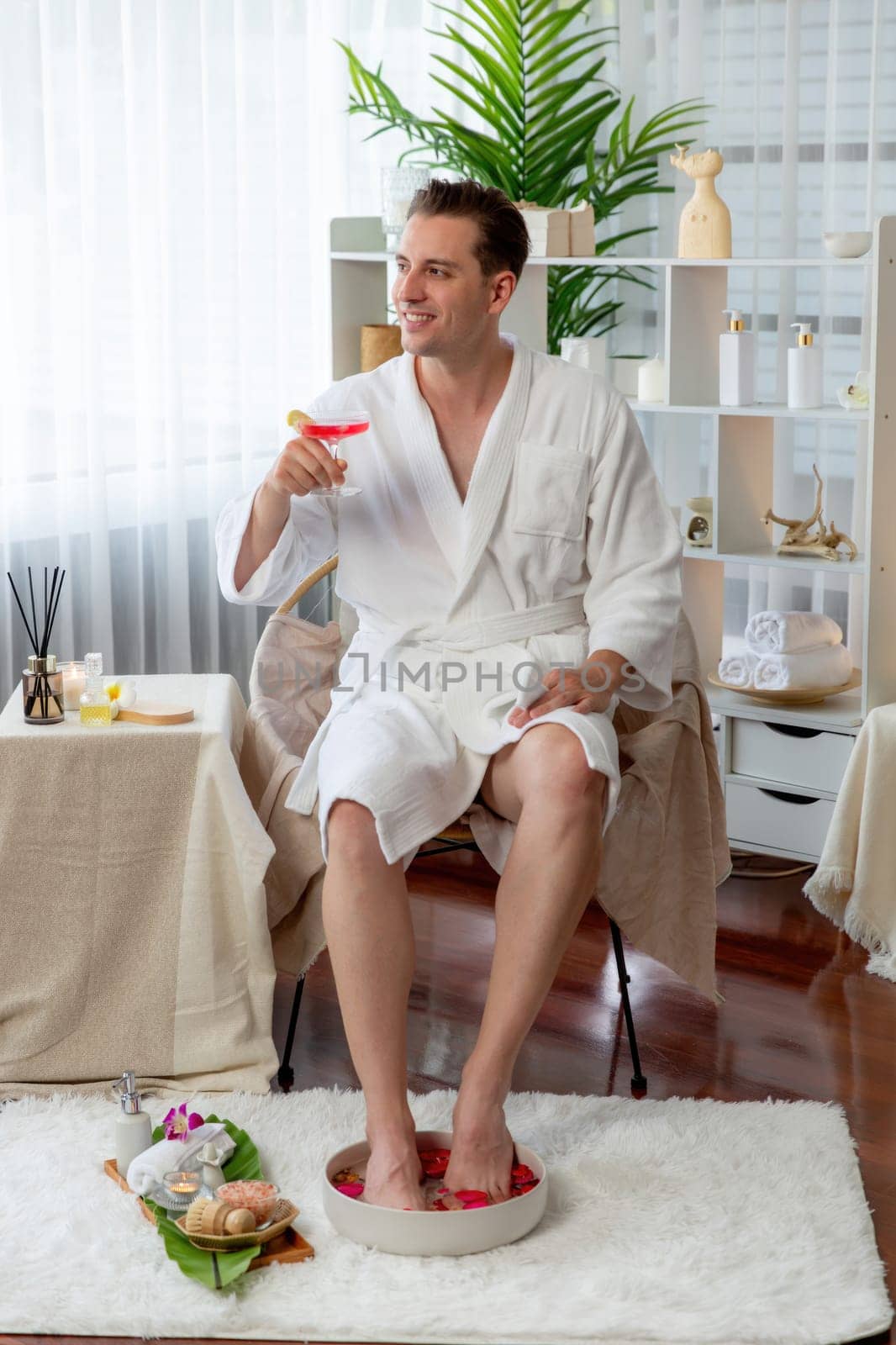 Beauty or body treatment spa salon vacation lifestyle concept with man wearing bathrobe relaxing with drinks in luxurious hotel spa or resort room. Vacation and leisure relaxation. Quiescent