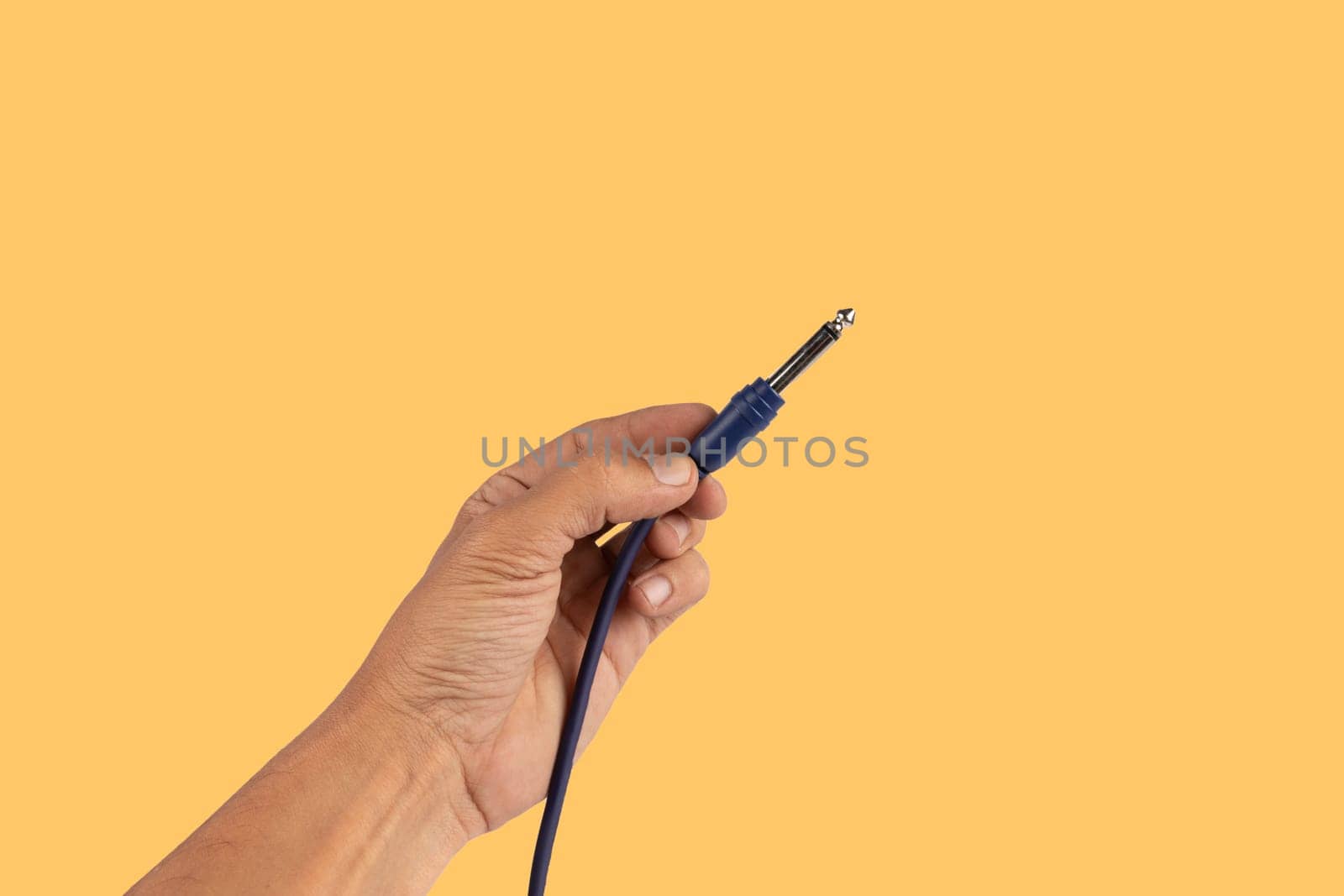 Black male hand holding an audio Jack cable isolated on yellow by TropicalNinjaStudio