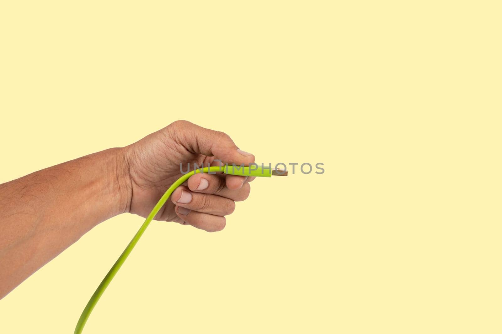 Black male hand holding a USB charger plug isolated on yellow background. High quality photo