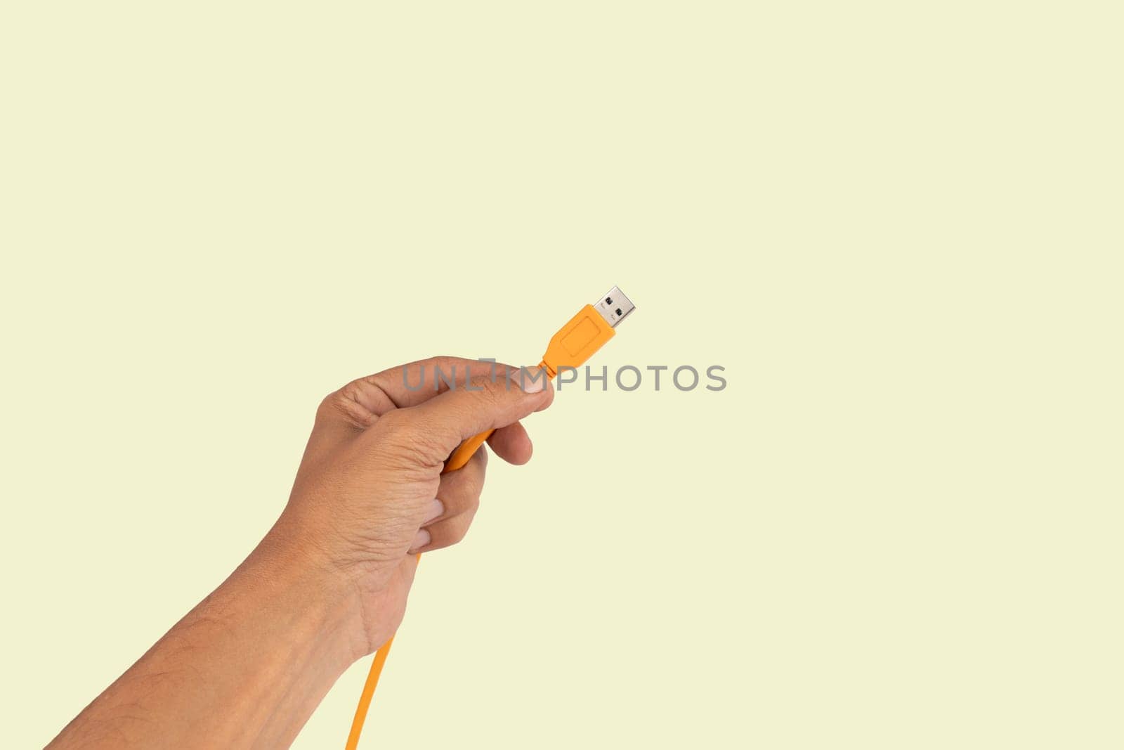 Black male hand holding an orange USB cable isolated on light green background by TropicalNinjaStudio