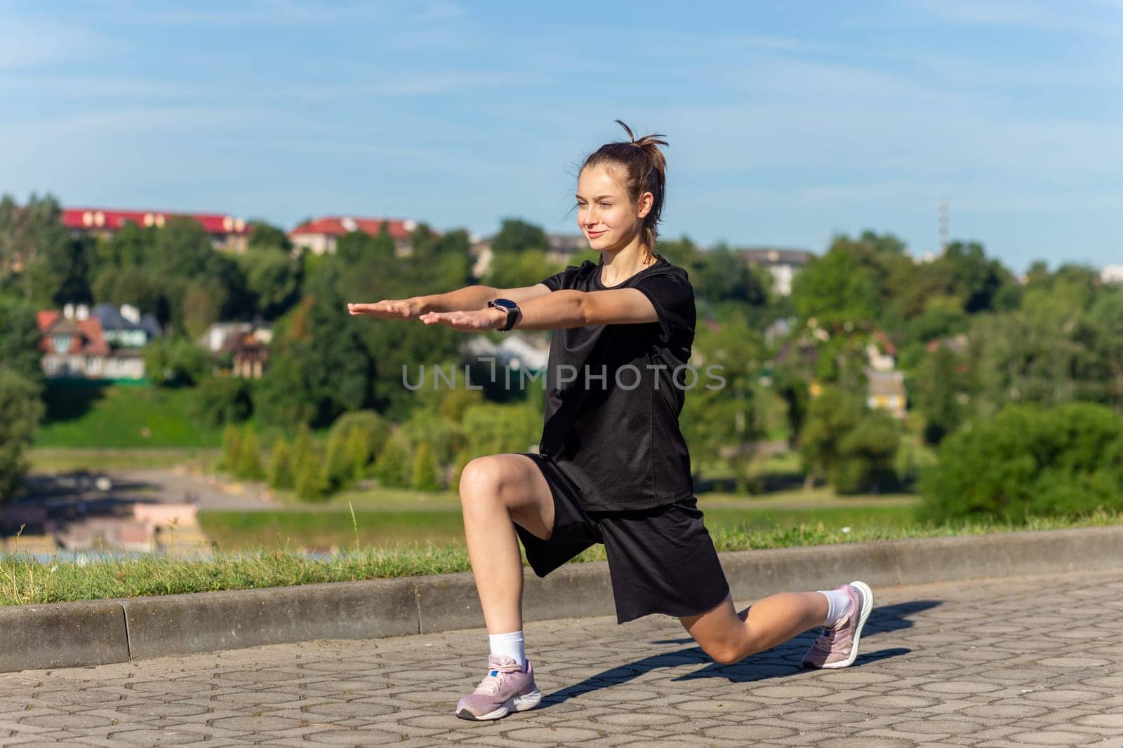 Young, fit and sporty girl in black clothes stretching after the workout in the urban city park. Fitness, sport, urban jogging and healthy lifestyle concept.