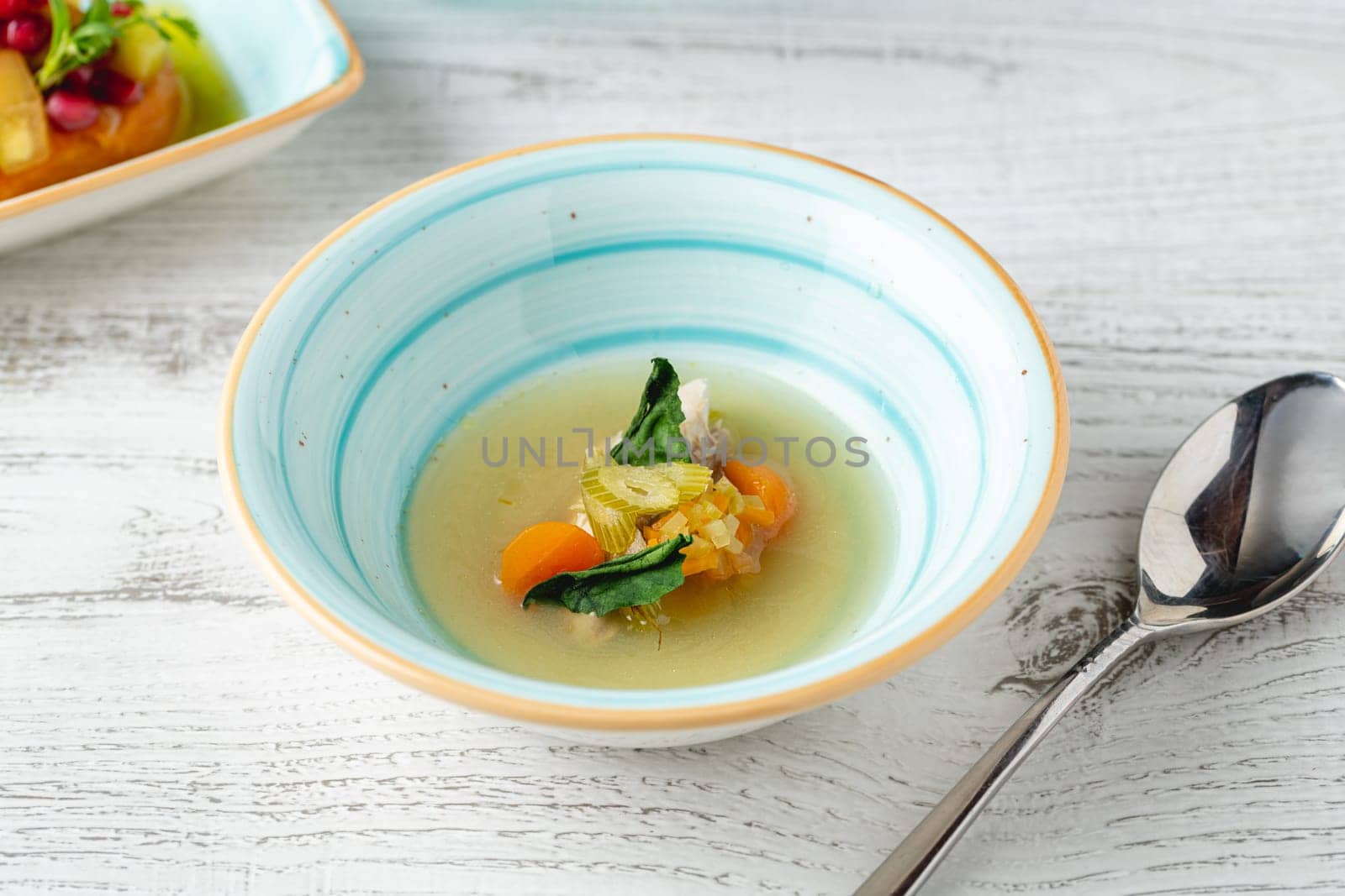 Fish soup with vegetables on white wooden table by Sonat