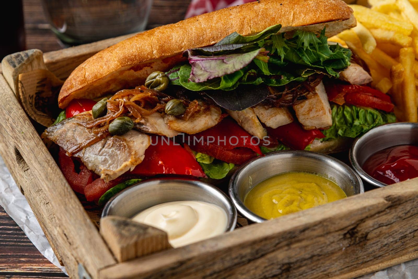 Steak sandwich with sauces and french fries on wooden table by Sonat