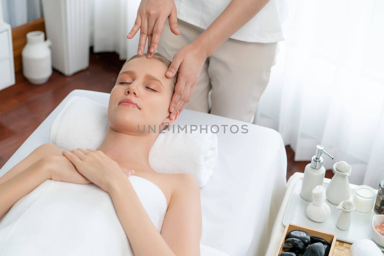 Caucasian woman enjoying relaxing anti-stress head massage and pampering facial beauty skin recreation leisure in dayspa modern light ambient at luxury resort or hotel spa salon. Quiescent