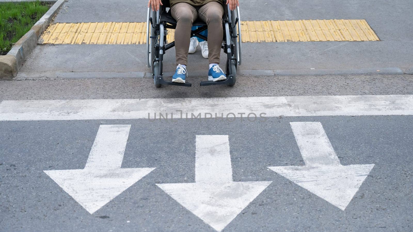 An elderly woman in a wheelchair is about to cross the road at a pedestrian crossing. by mrwed54