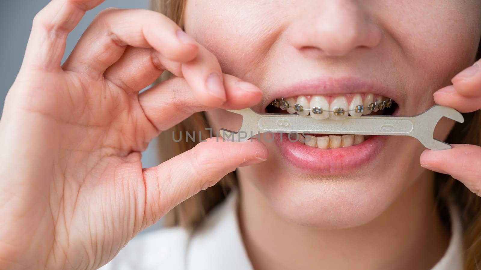 Close-up portrait of a woman with braces holding a wrench in her teeth