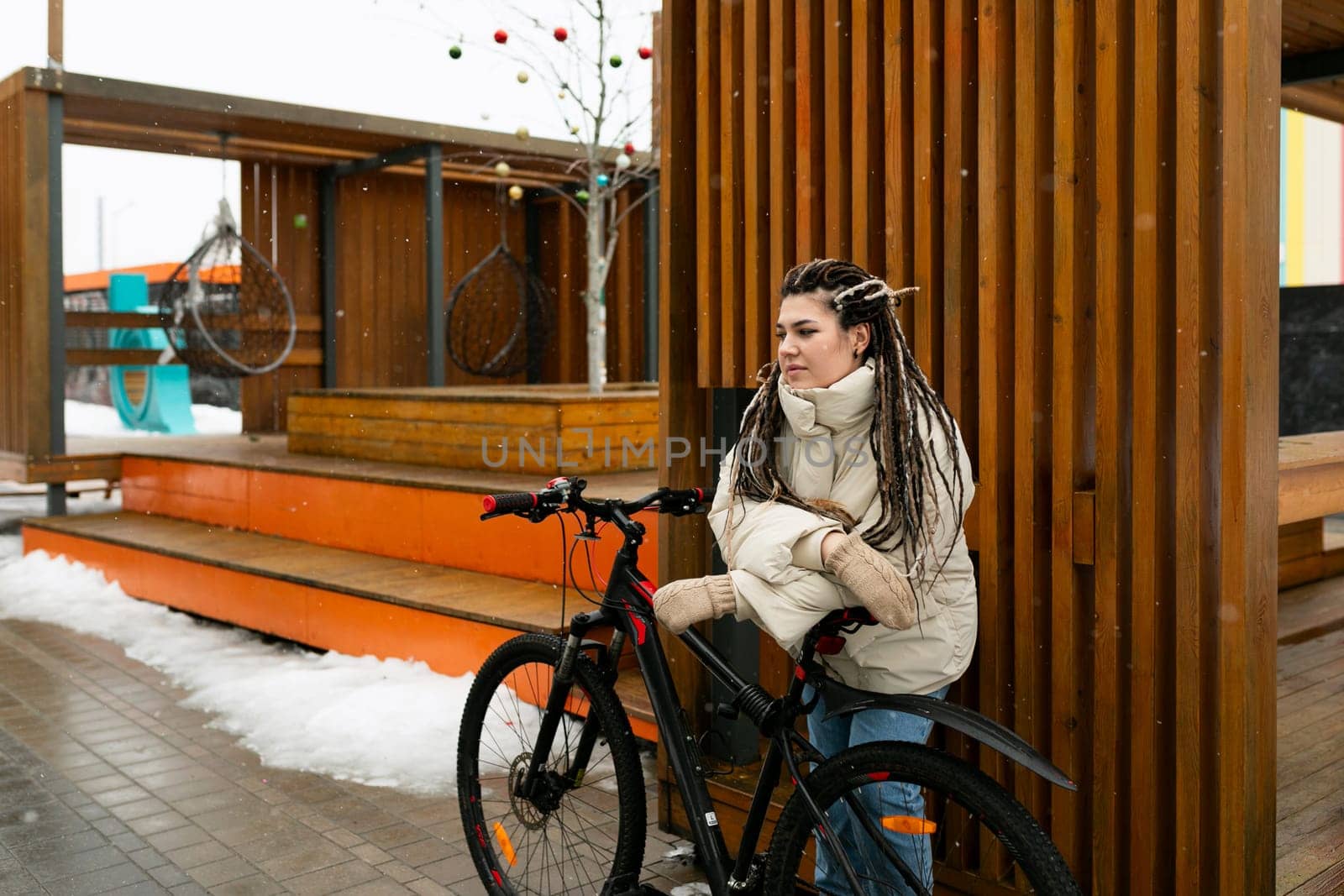 A woman with dreadlocks is casually seated on a bike, with a relaxed posture. She appears confident and comfortable as she balances herself on the bicycle.