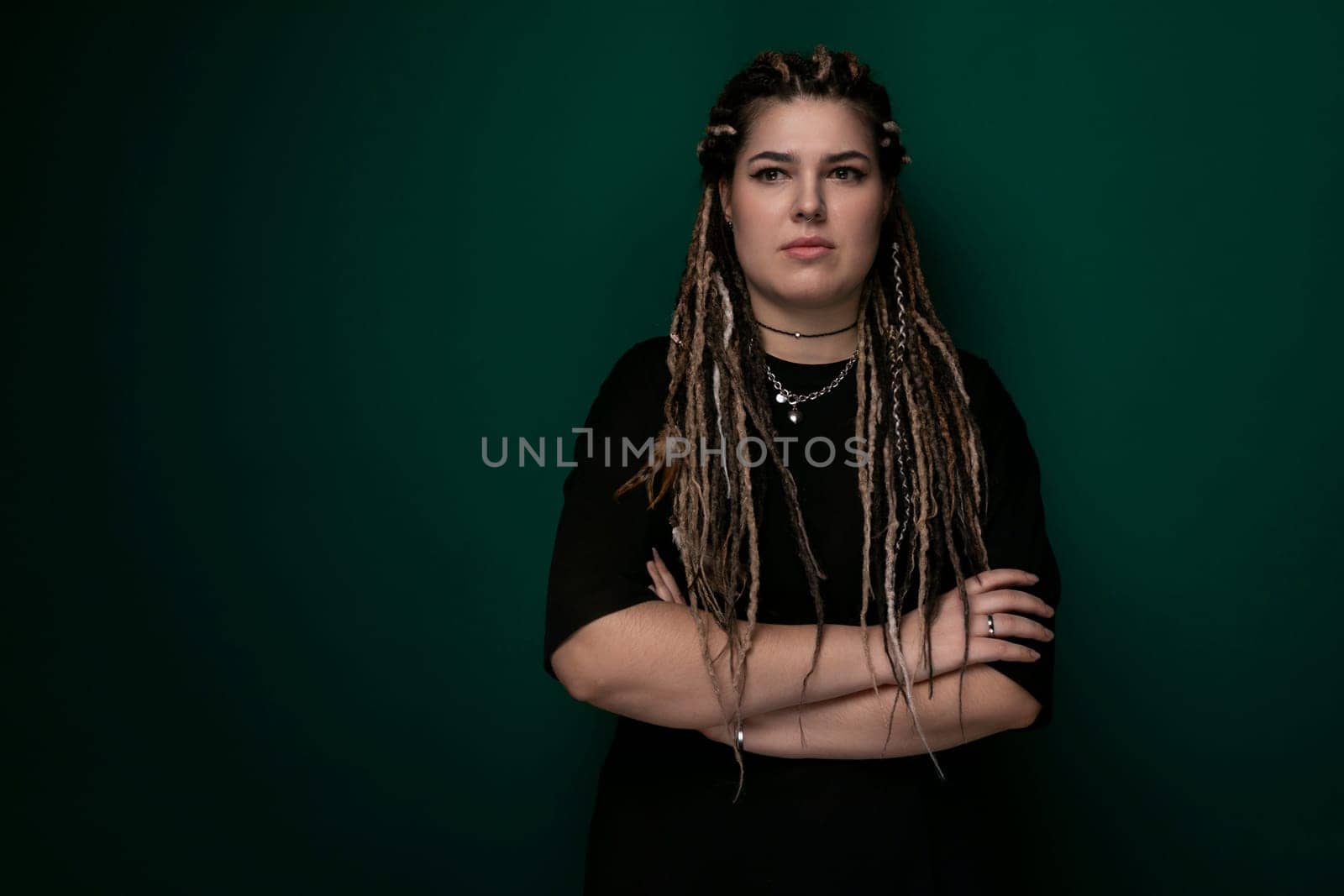 A woman with dreadlocks is standing upright, with her arms confidently crossed over her chest. She is looking directly ahead, displaying a strong and assertive posture.