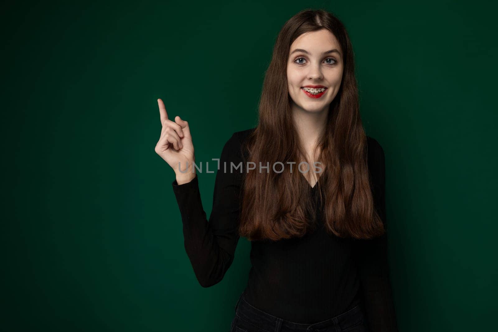 A woman wearing a black shirt is raising her hand to make a peace sign gesture. Her fingers are forming the V-shape commonly associated with peace and victory signs.