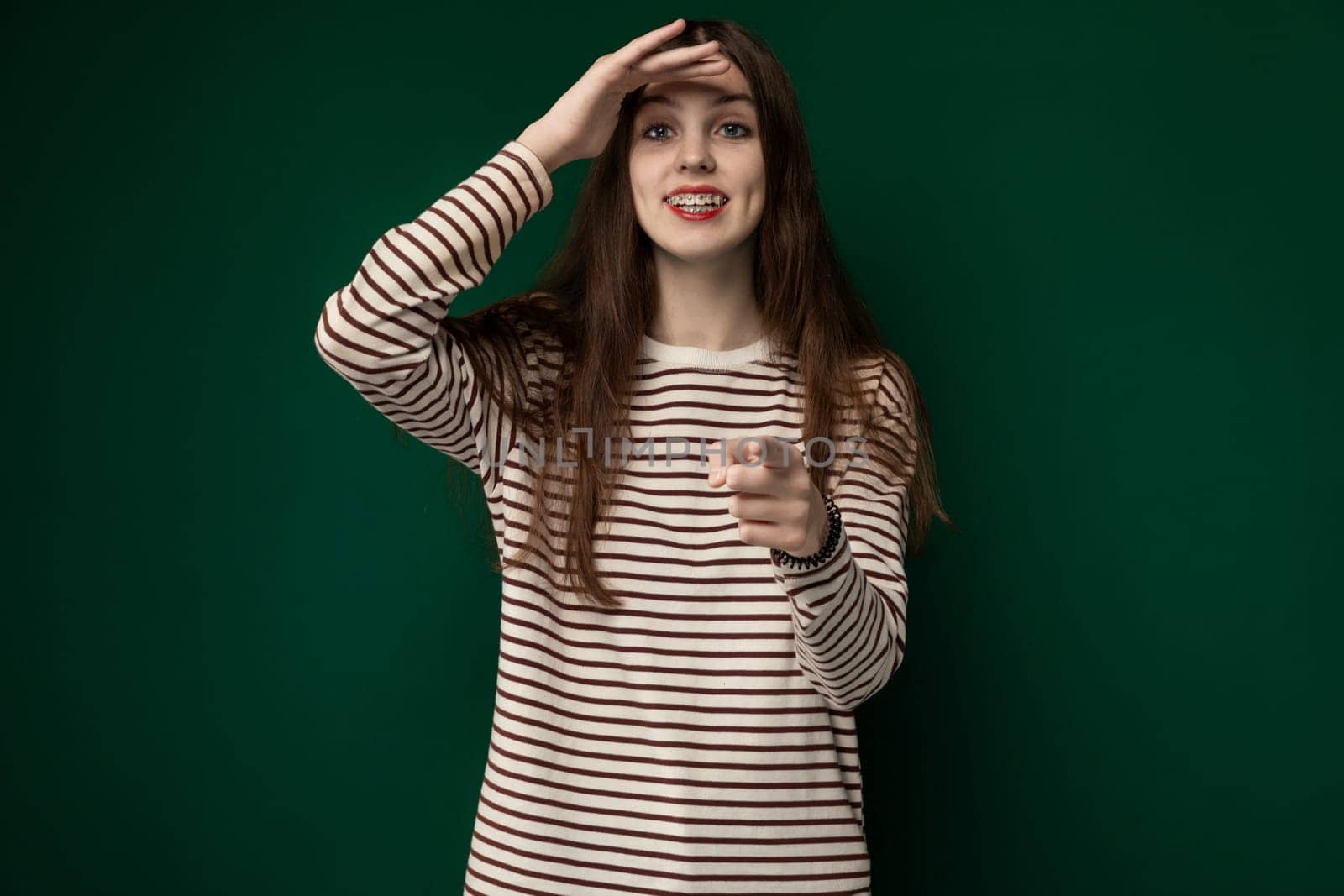A woman wearing a striped shirt is shown in distress as she holds her head with her hands, indicating she may be experiencing a headache or stress.