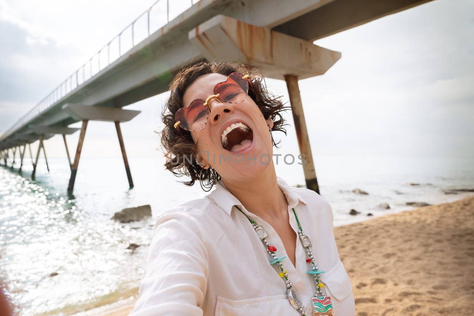 Front view of a caucasian woman wearing sunglasses on vacation by the sea laughing greeting by video call to a family member