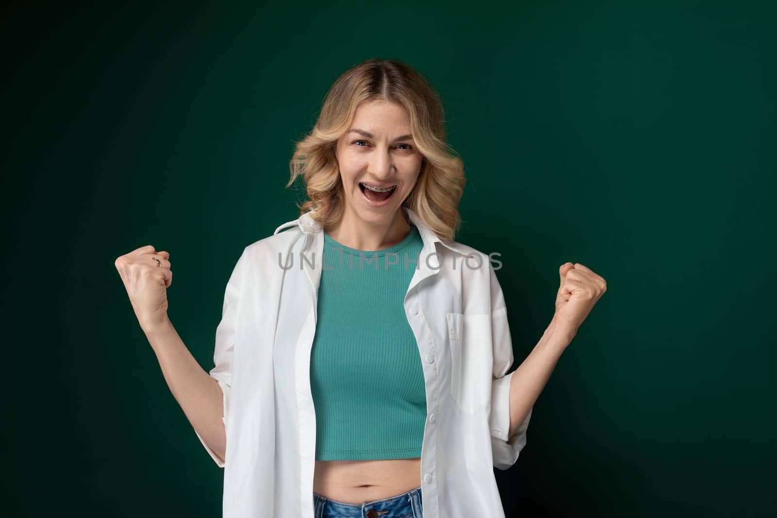 A woman dressed in a green top and white jacket standing outdoors. She looks stylish and confident as she poses for a photo.