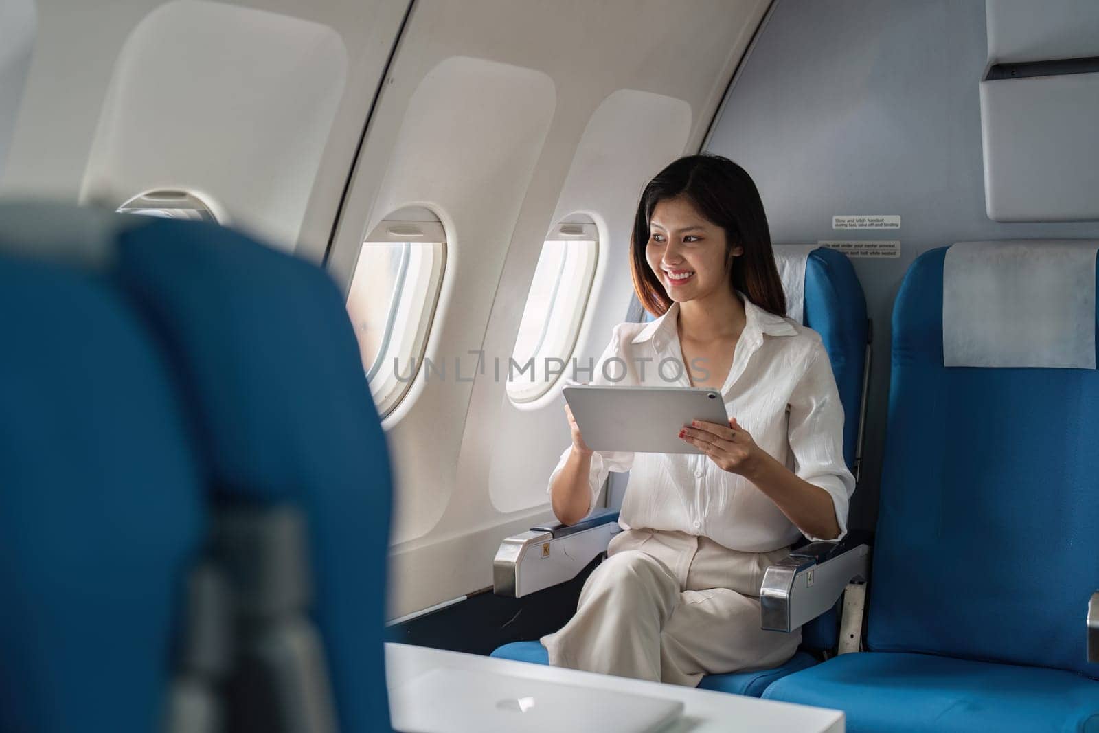 Business professional using a tablet on a modern airplane, showcasing a comfortable and efficient in-flight workspace for corporate travel.