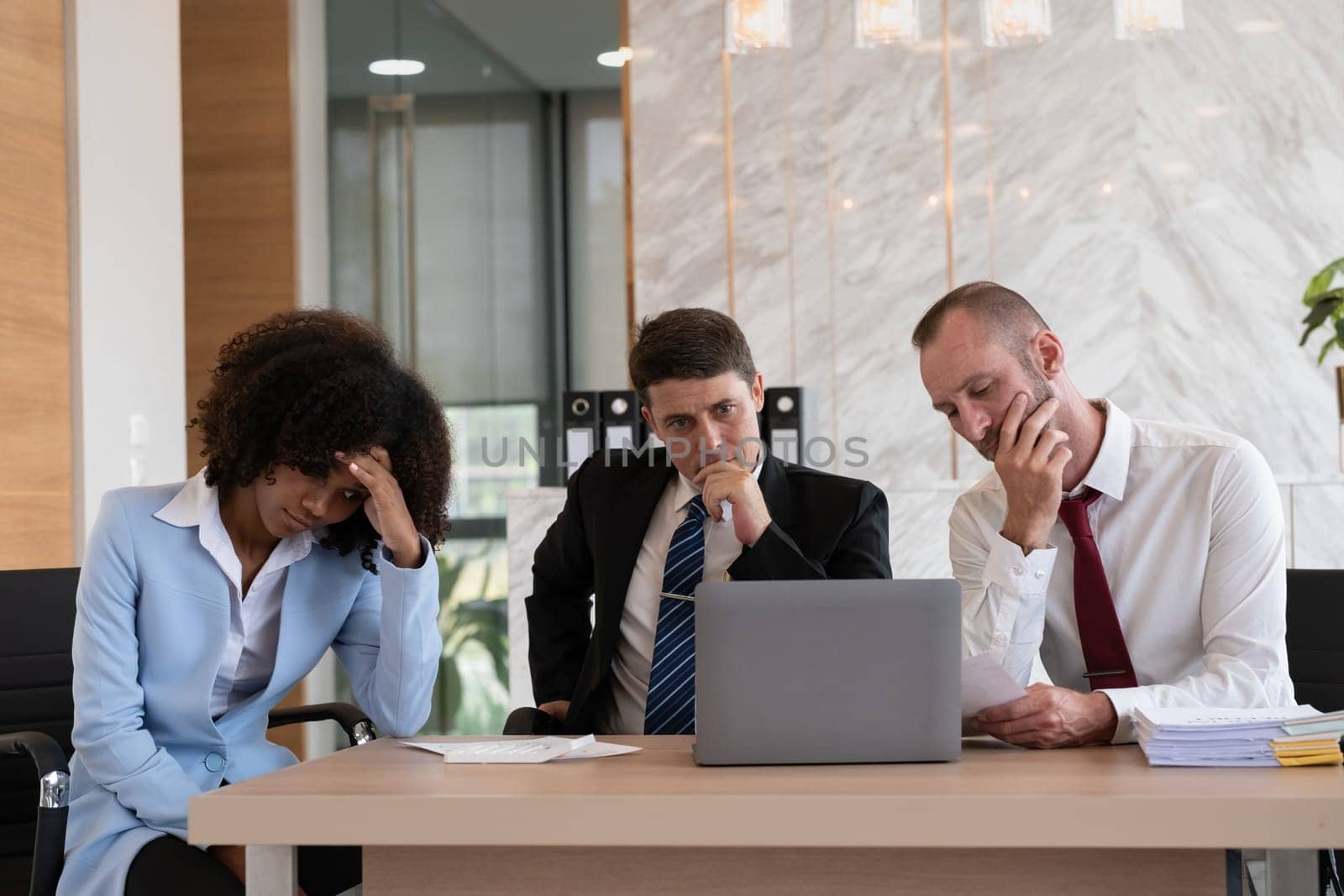 Diverse business team of three people, including a woman and two men, deep in thought at an office desk, modern office setting, Concept of strategic decision-making