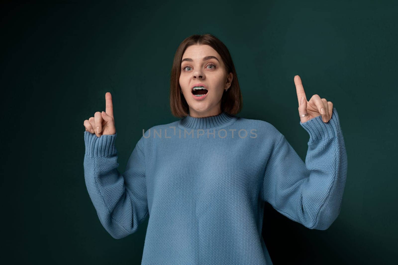 A woman wearing a blue sweater is contorting her face in a comical and unusual manner, showcasing a facial expression that appears strange yet humorous.