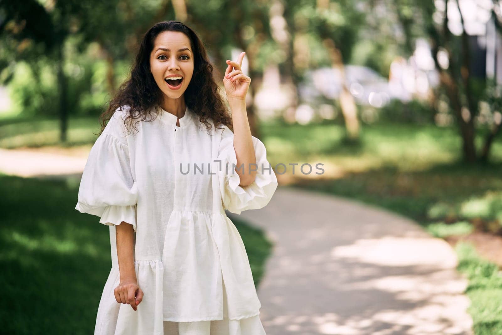 Cheerful curly-haired brunette girl with open mouth raises her index finger. Girl has an idea. High quality photo