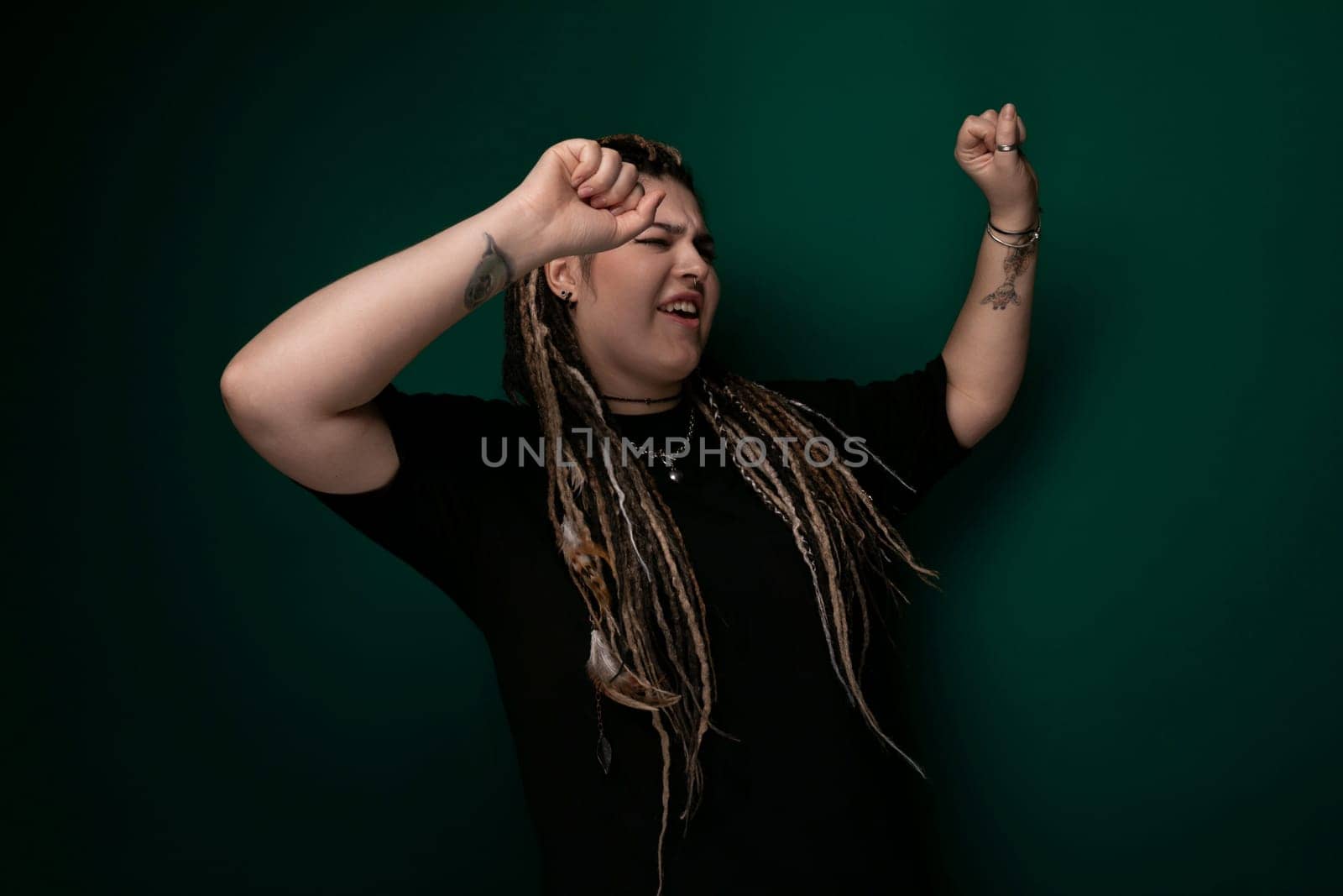 A woman with long dreadlocks wearing a black shirt. She is standing confidently, her hair neatly styled. The background is simple, allowing her to stand out.