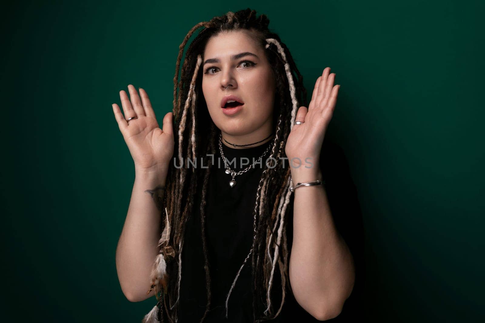 A woman with dreadlocks standing confidently in front of a vibrant green wall. Her colorful hair stands out against the background, creating a striking visual contrast.