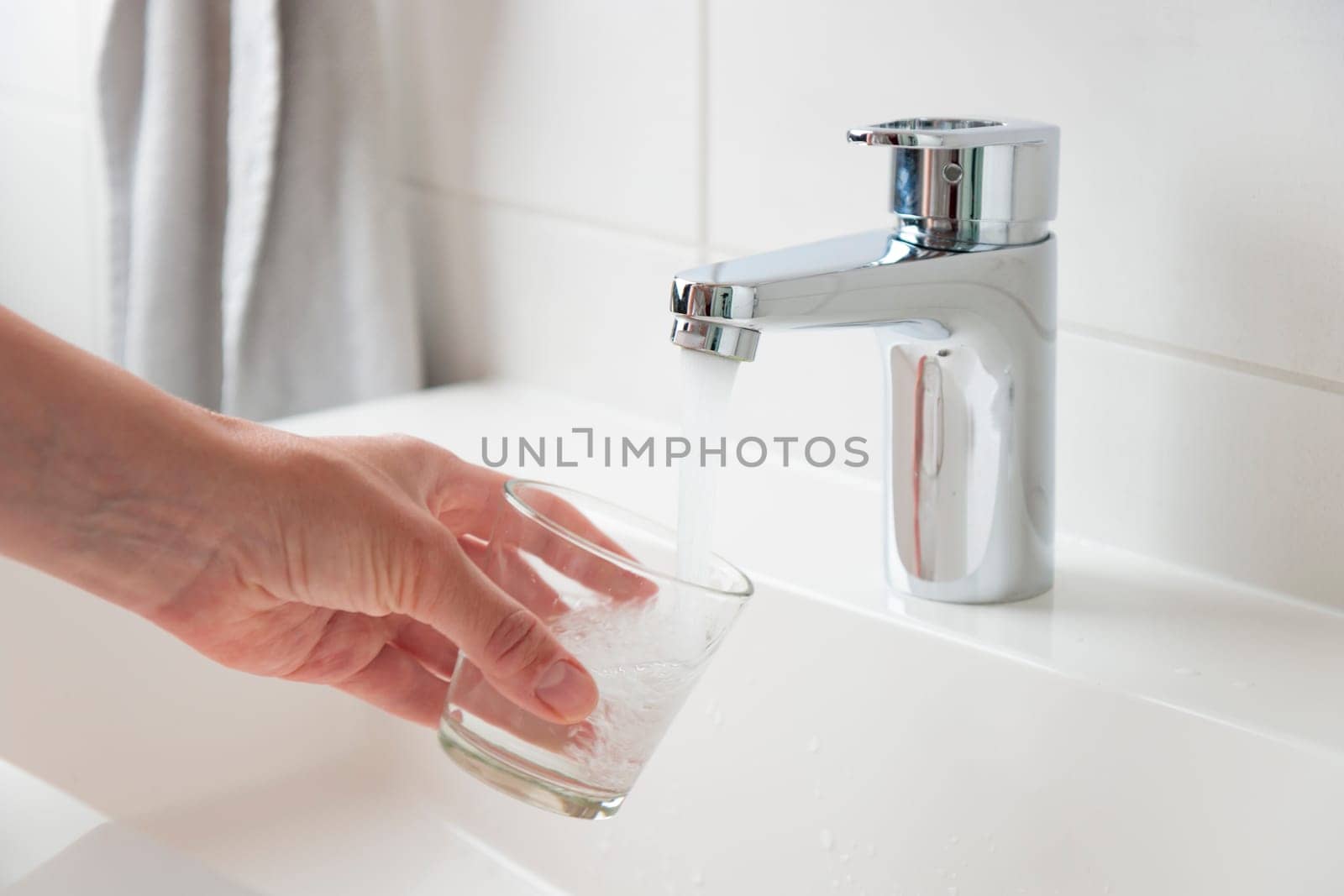 Woman filling glass with tap water from faucet in bathroom, closeup. Concept of clean drinking tap water