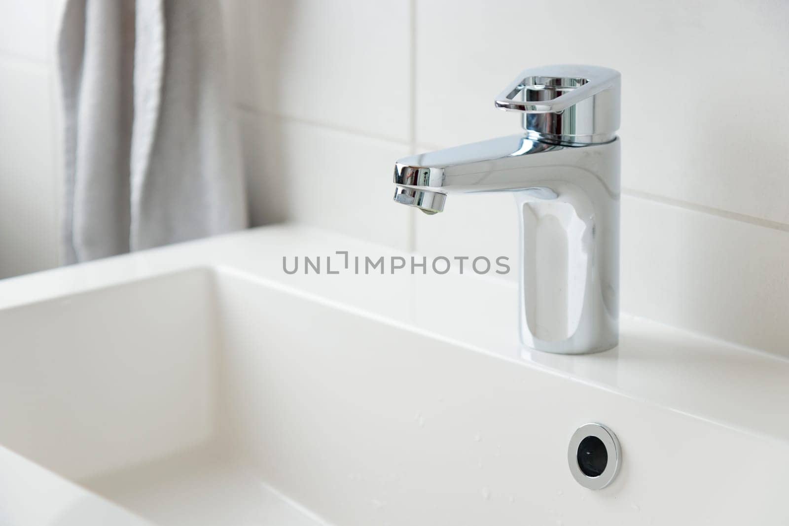 A drop of pure water dripping from the tap in the white modern bathroom. Clean tap water concept. Wise use of natural resources.