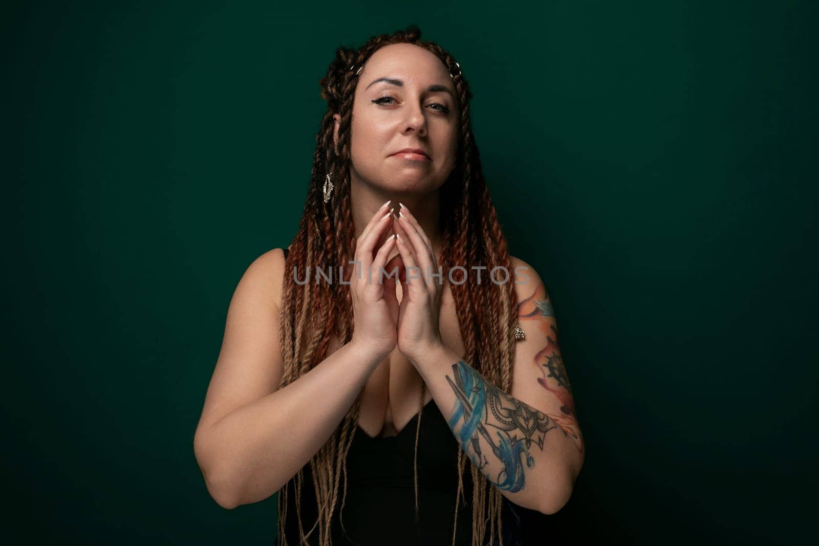 A woman with dreadlocks is standing confidently in front of a vibrant green background. Her hair is styled in long, thick dreadlocks, and she has a serene expression on her face.