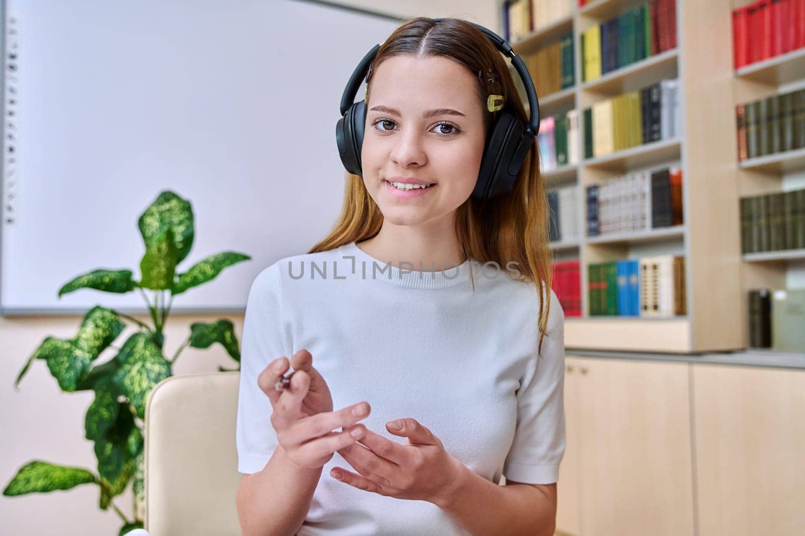 Webcam view of teenage girl, high school student, in headphones, talking to camera. Female teenager studying remotely, video conference chat, online test exam lesson. Technology education adolescence