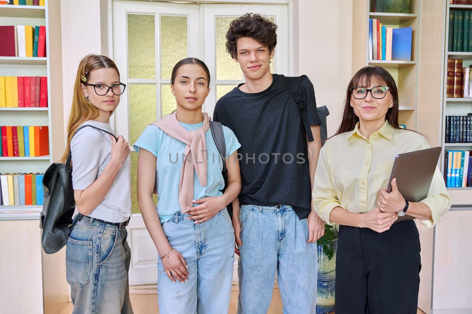 Portrait of group of teenage students with female teacher looking at camera in classroom library. High school, education, adolescence, teaching, learning concept