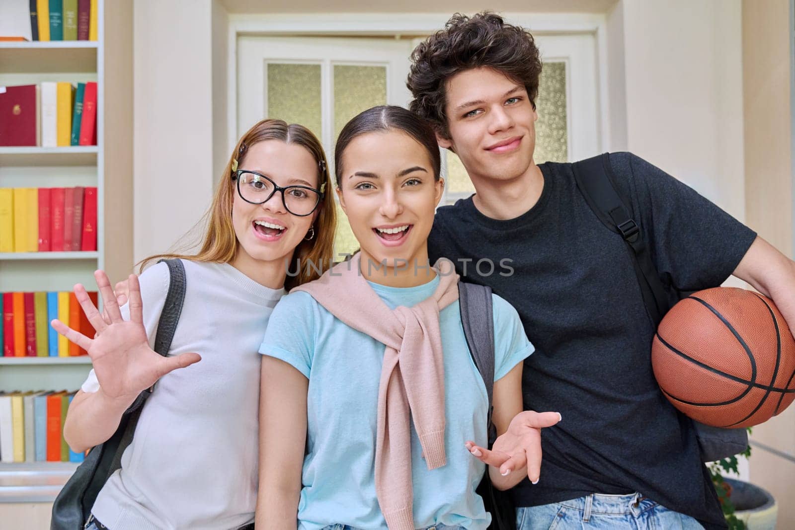 Three cheerful smiling teenagers friends students looking at camera inside high school classroom campus. Adolescence, friendship, education, 17-18 years old students, teenage concept