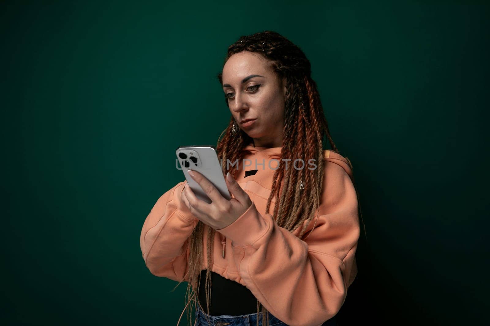 A woman with dreadlocks, wearing casual clothing, is looking intently at a cell phone screen in her hands. Her facial expression suggests focus and engagement with the device.